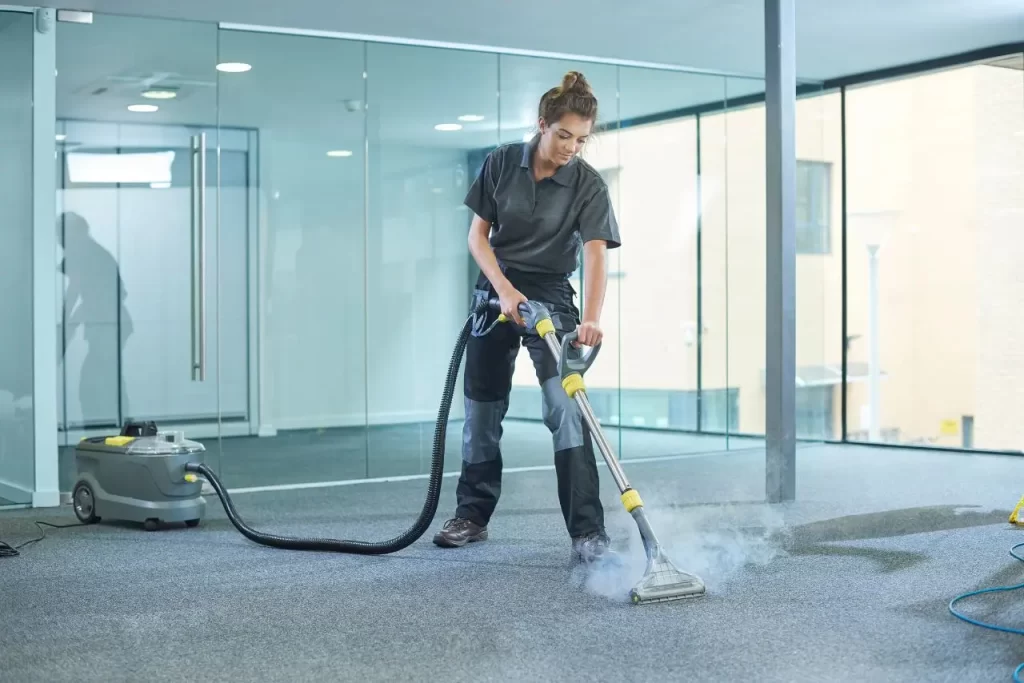 Woman using a steam cleaning machine on an office carpet as part of a deep commercial carpet cleaning service.