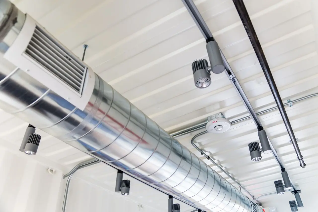 Metallic spiral air duct with spotlights and smoke detector mounted on a modern industrial ceiling