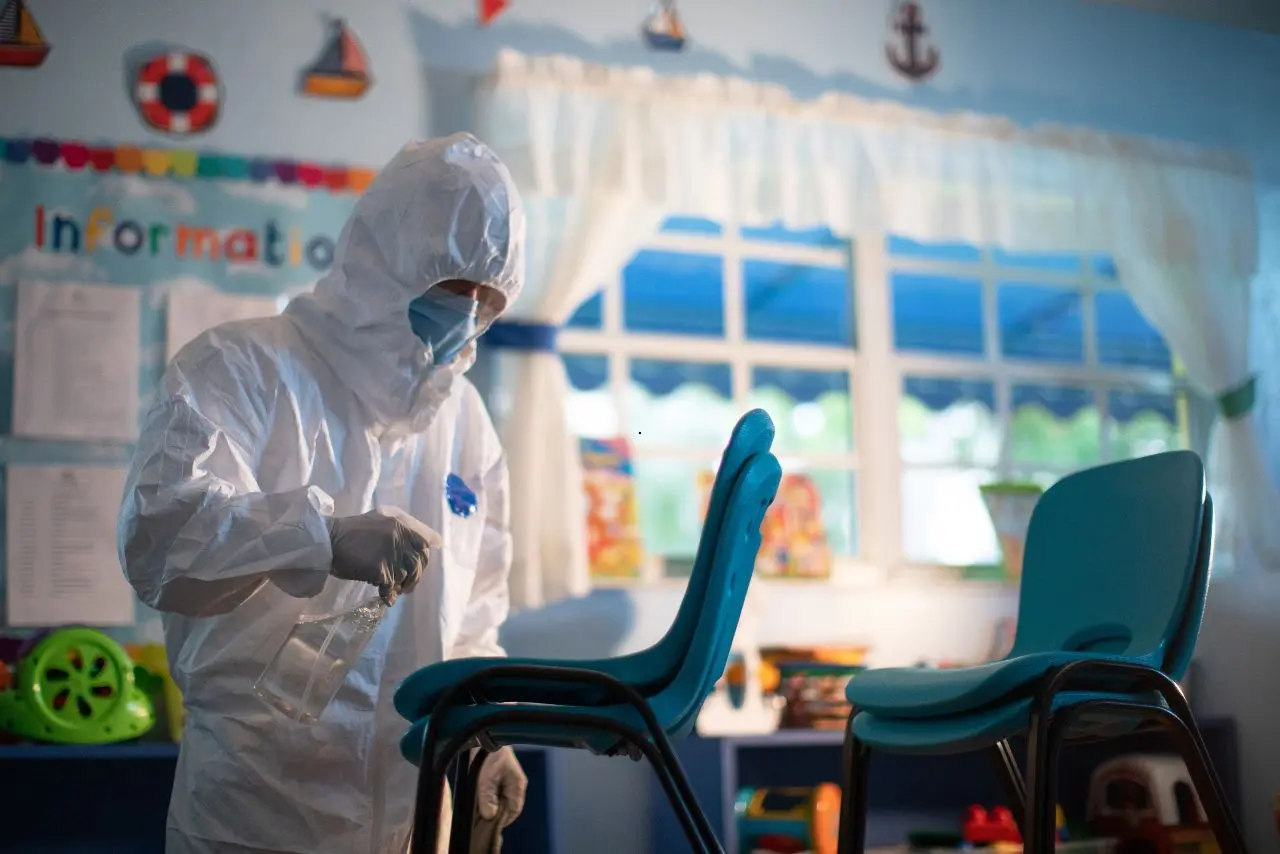 Professional in full PPE disinfecting chairs in a daycare classroom as part of daycare cleaning services.