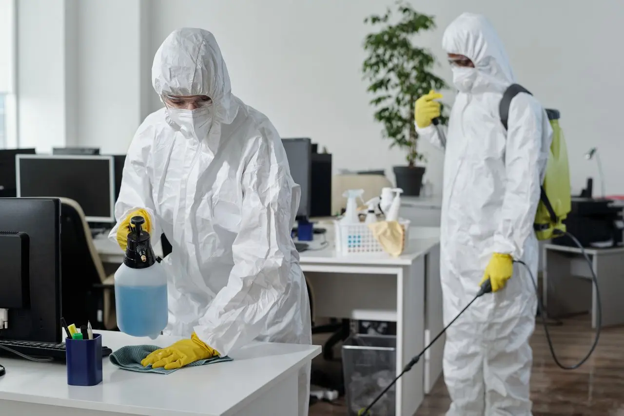Technicians in full protective suits disinfect office surfaces with spray and fogging equipment—showcasing expert disinfection services in action.
