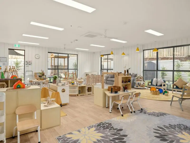 Spacious and clean daycare classroom with wooden floors, colorful toys, learning stations, and cozy seating areas.