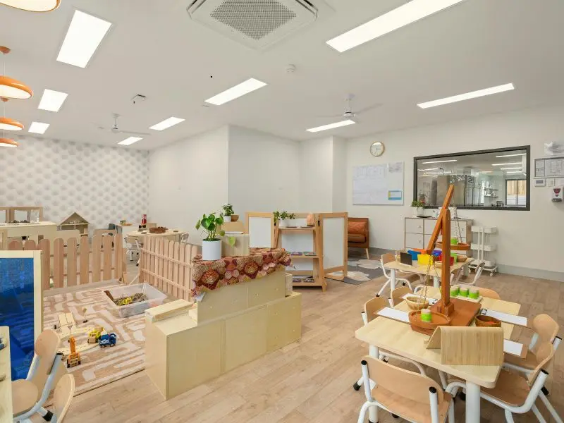 Organized and brightly lit daycare classroom with clean wooden floors, toys, and learning stations.
