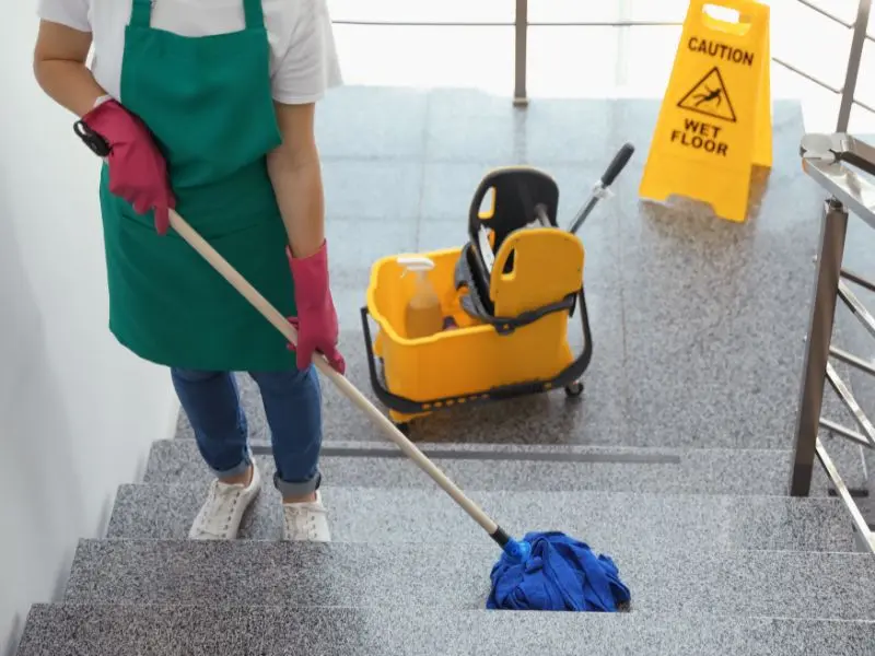 Worker mops granite stairs with caution sign visible, highlighting safe commercial cleaning practices. Prevent slips and ensure cleanliness.