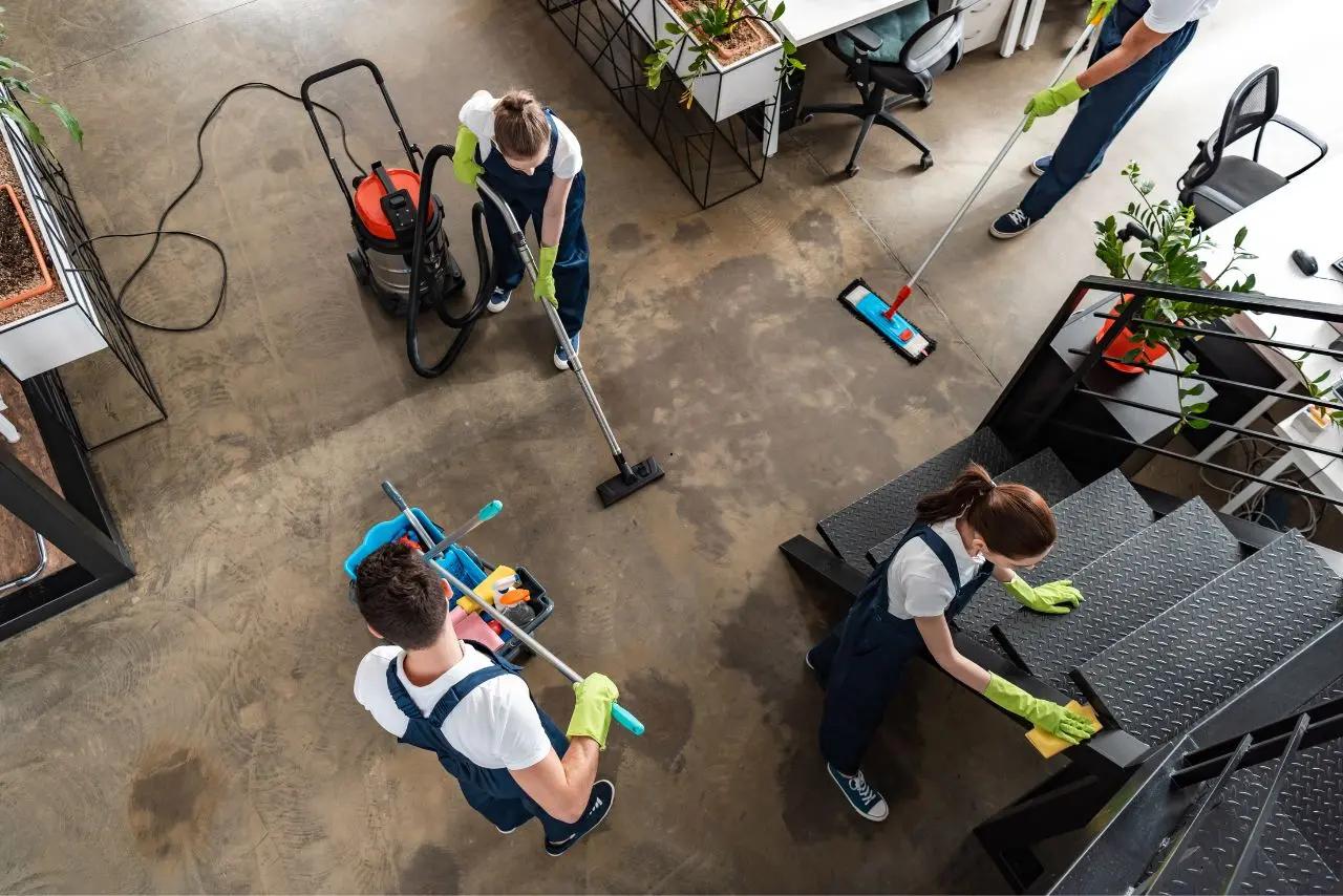 Four-person cleaning team sanitizing office stairs and floors with vacuum, mop, and cart of supplies.