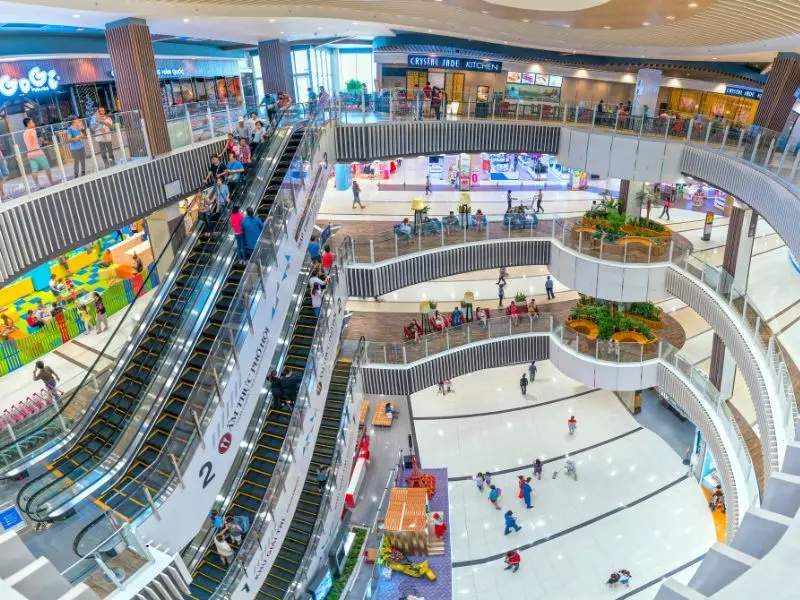 Bright and spacious multi-level shopping mall with clean floors, escalators, and active shoppers.