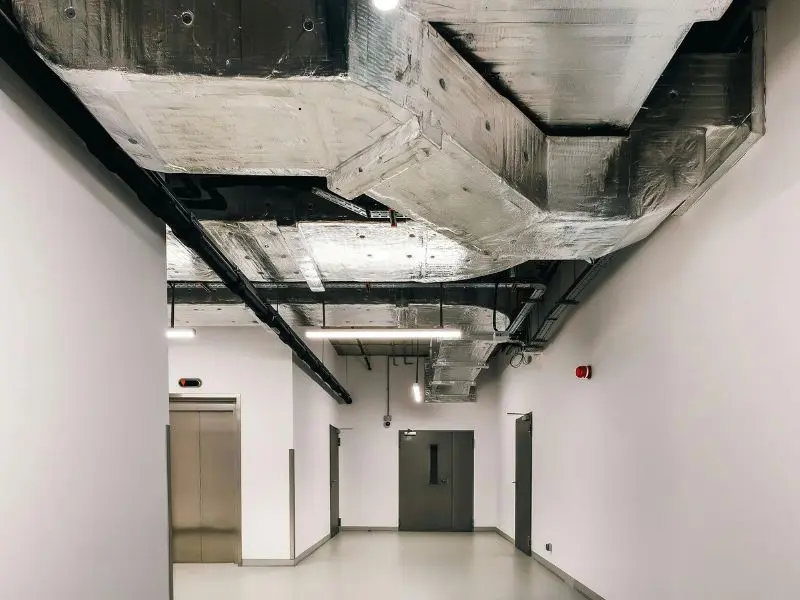 Large insulated air ducts run across the ceiling of a clean, modern commercial hallway with white walls