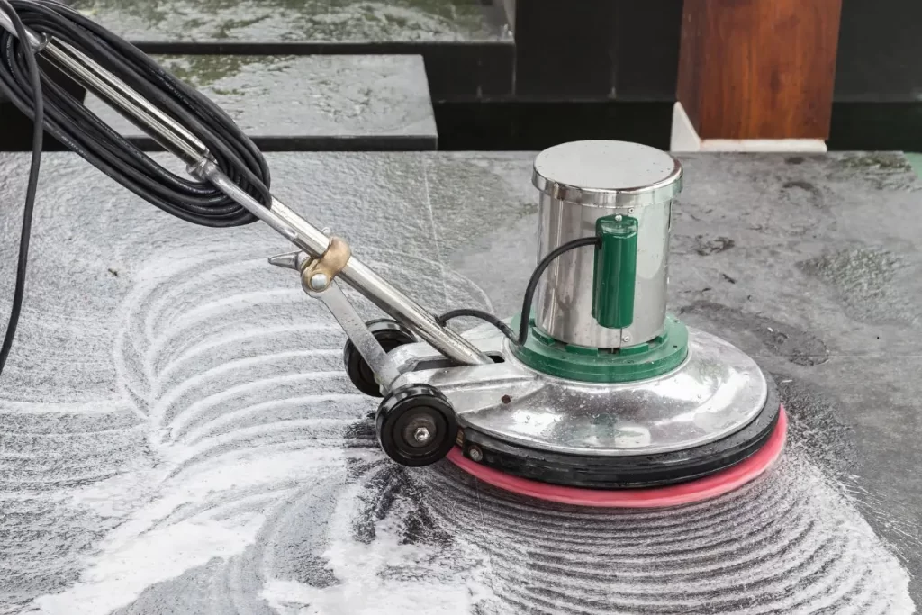 Close-up of a floor buffer machine scrubbing a surface with foam during a professional floor stripping and waxing process for shine.