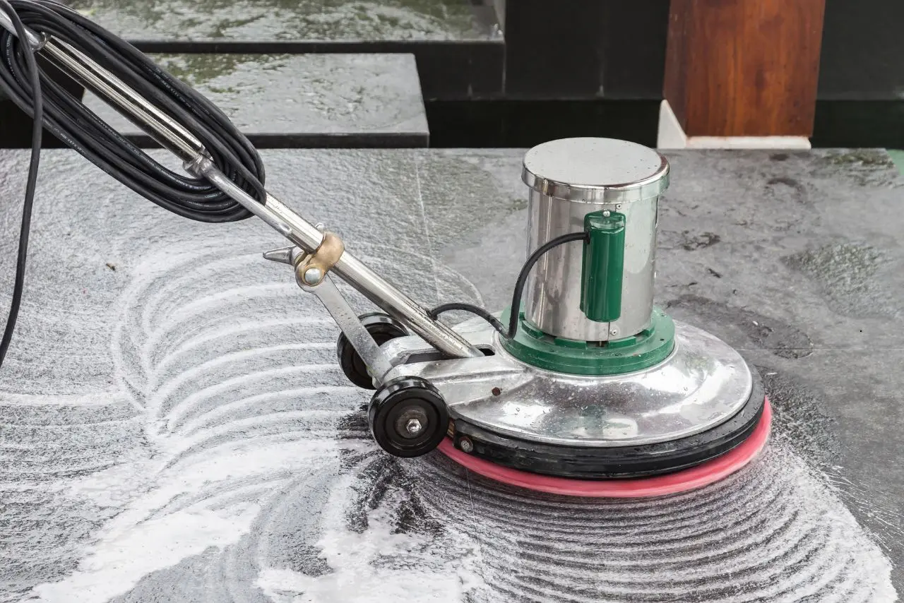 Close-up of a floor buffer machine scrubbing a surface with foam during a professional floor stripping and waxing process for shine.