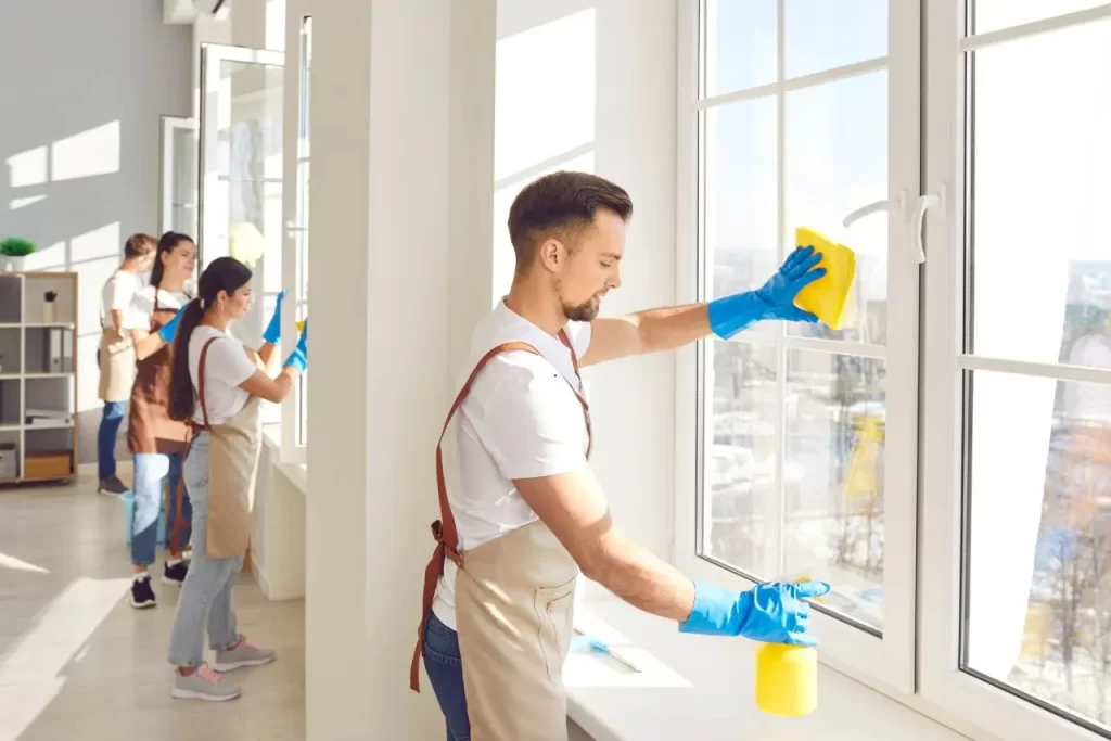 Group of professional cleaners wiping large windows with gloves and sponges in a sunny office