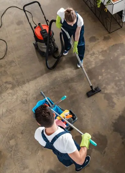 Two professional cleaners using vacuum and mop to clean a concrete floor