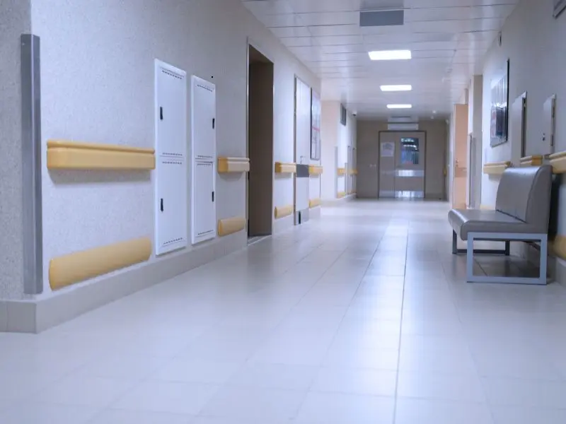 Sanitary hospital hallway with tiled floors, seating area, and clean walls maintained for a hygienic healthcare environment.