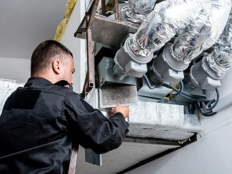 Worker performs HVAC maintenance by cleaning ducts and inspecting a commercial ventilation system.