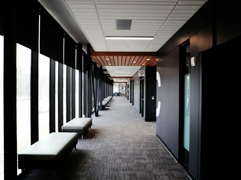 Commercial hallway with carpet flooring, benches, and tall windows.