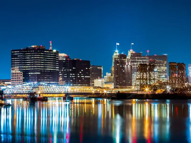 Illuminated Newark skyline and bridges reflecting vibrant city lights over the calm river at night.