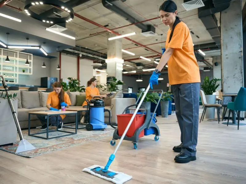 Professional cleaners in uniform sanitize a modern office space with mops and equipment, ensuring a spotless and healthy work environment.