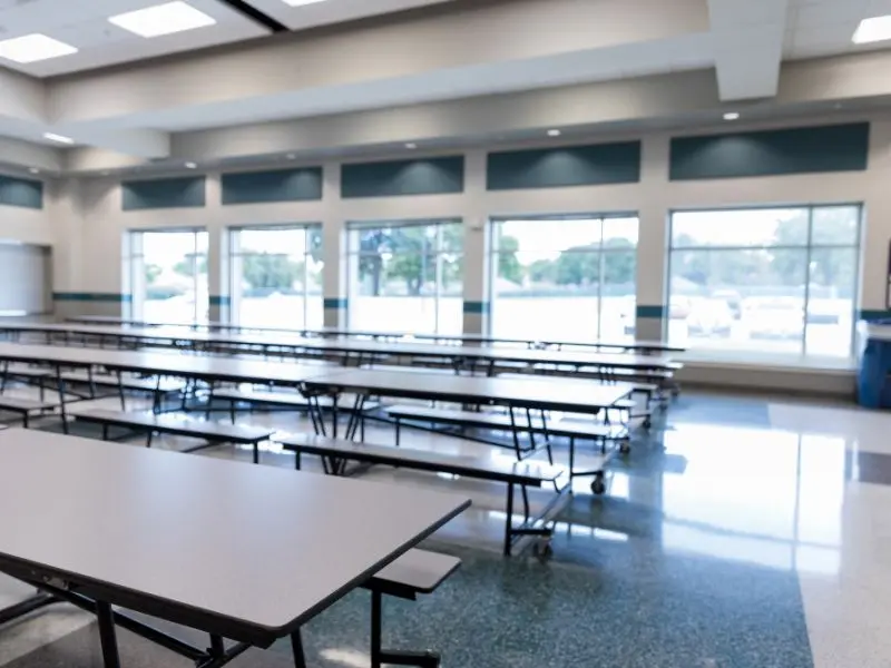 Spacious school lunchroom with large clean windows, polished floors, and empty lunch tables.