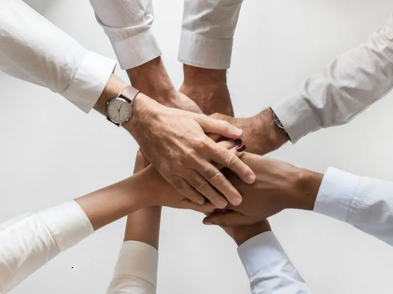 Group of six people placing their hands together in the center, symbolizing unity, trust, and collaboration.