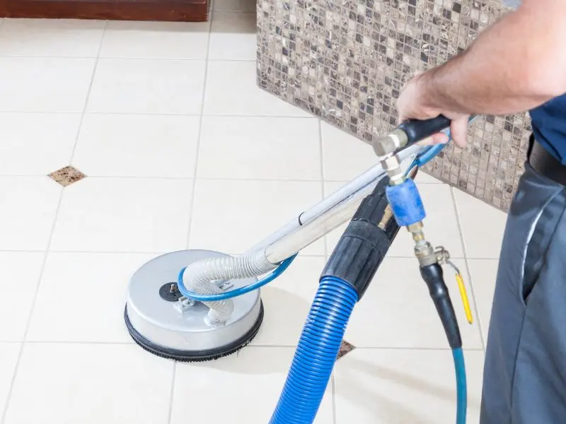 Technician using floor cleaning machine on tiled surface with grout lines.