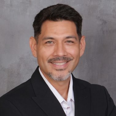 Smiling man in a black blazer and white shirt posing in front of a gray background