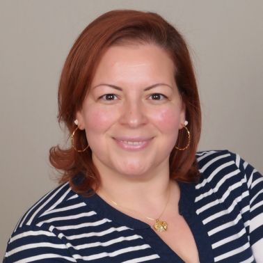 Woman with red hair and striped shirt smiling at the camera in a neutral setting