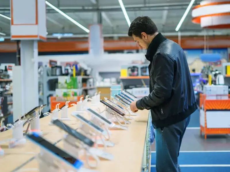 Man in leather jacket exploring tablet options on display at a technology retail store