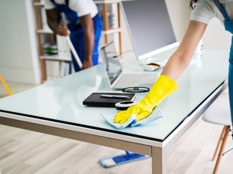 Office cleaning tips shown as workers sanitize desks with gloves and microfiber cloths