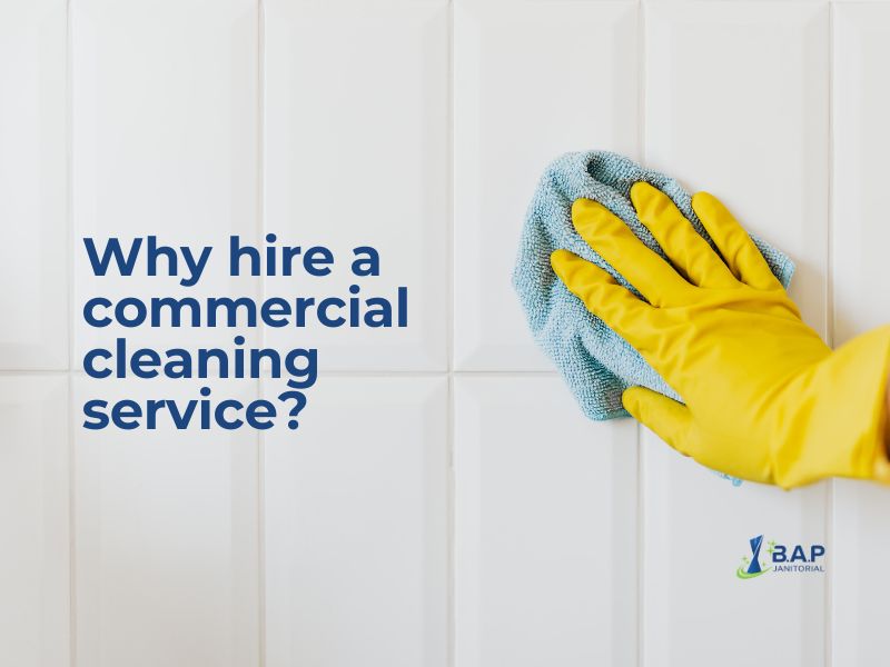 Why hire a commercial cleaning service shown by a gloved hand wiping white tiled surfaces with a microfiber cloth in a professional cleaning setting.