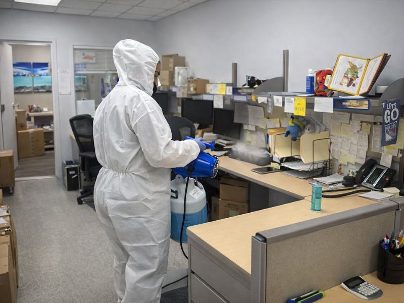 Technician performing electrostatic disinfection services in office workspace using electrostatic sprayer equipment