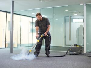 Professional technician performing carpet deep cleaning with steam extraction equipment in a modern office space.